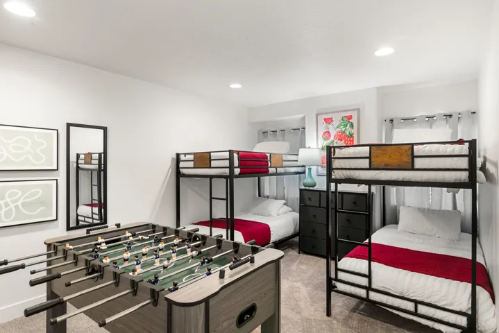 Recessed lighting illuminates a room featuring two metal-frame bunk beds, a foosball table, and neutral-toned carpeting