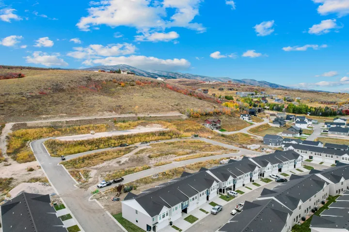 Developing residential community featuring a paved street system, new construction townhomes with dark shingle roofs, and open land for future development