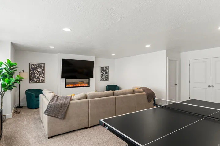 Entertainment space featuring recessed lighting, carpet flooring, a wall-mounted television above an electric fireplace, and paneled doors