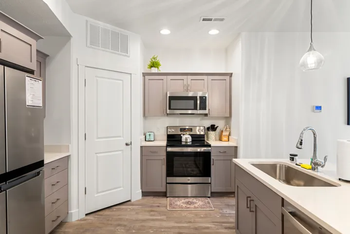 Kitchen featuring wood-finish flooring, stainless steel appliances including a refrigerator, range, and microwave, light-toned cabinetry, and a kitchen island with an undermount sink
