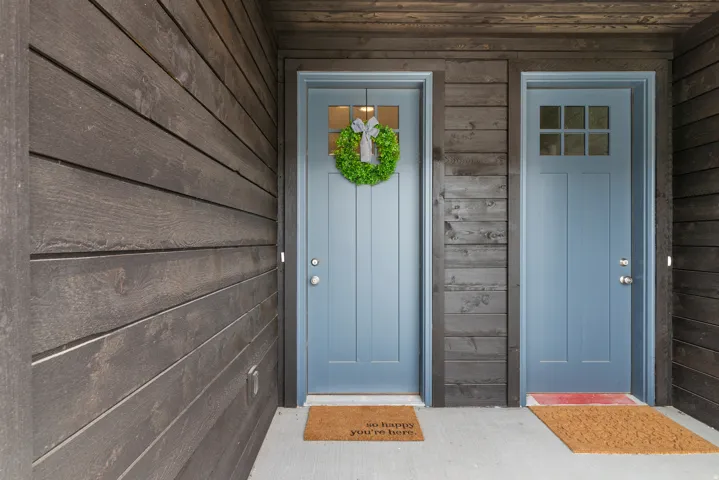Entryway featuring two light blue panel doors with window inserts, set against dark wood-finish horizontal siding