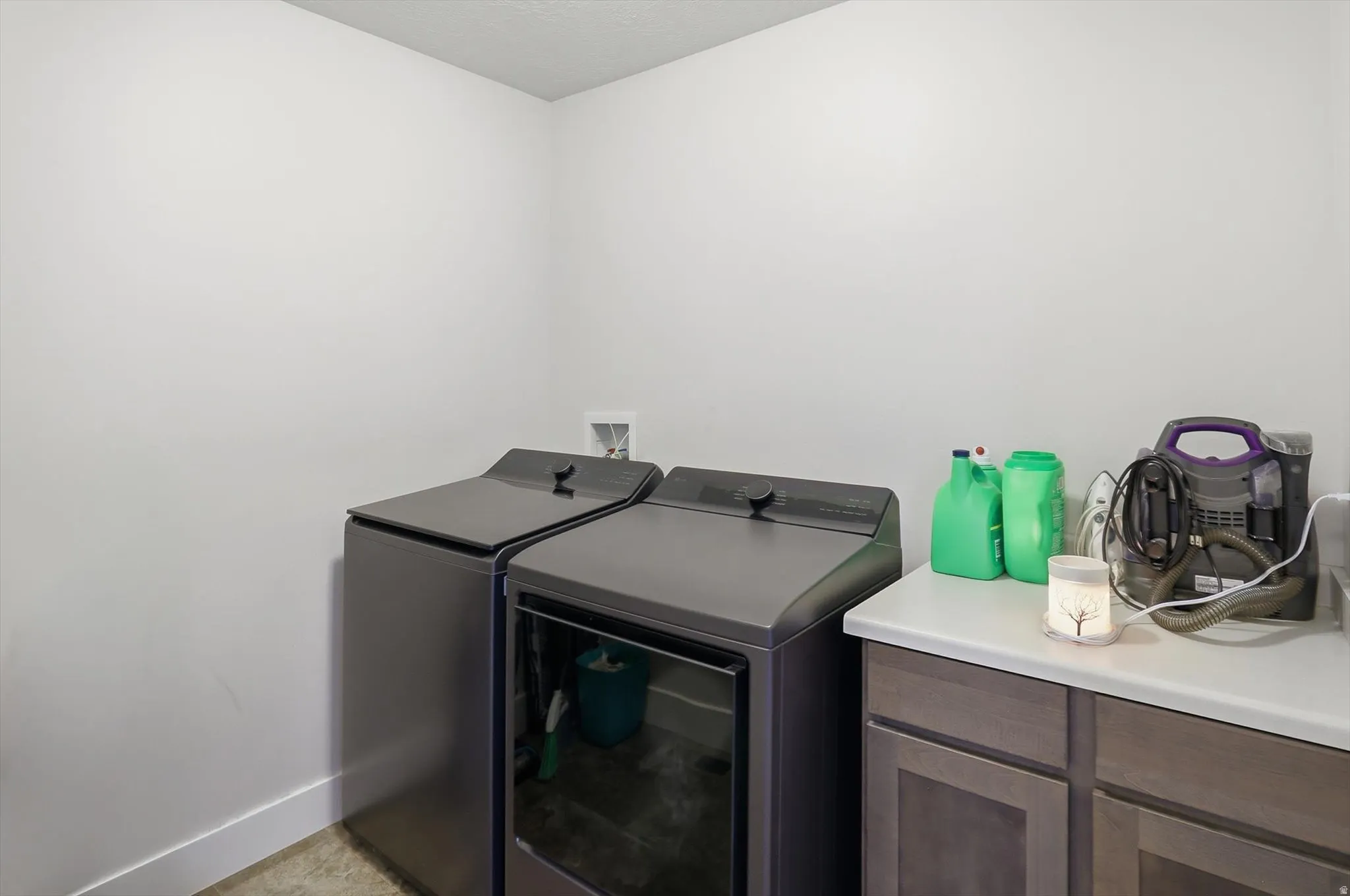 Laundry area featuring light-toned walls, a white baseboard, and a built-in cabinetry unit with a light-colored countertop