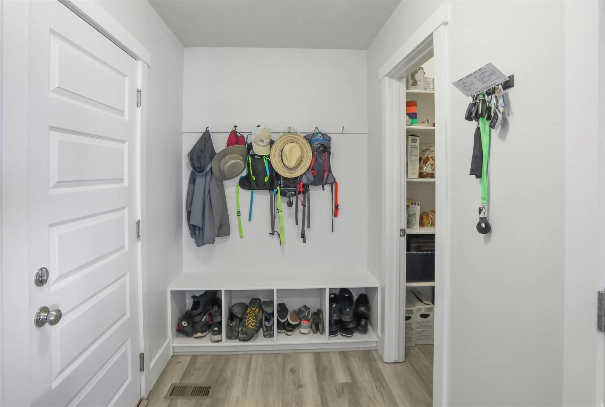 Entryway featuring wood-finish flooring, a white paneled door, and built-in storage bench with individual cubbies
