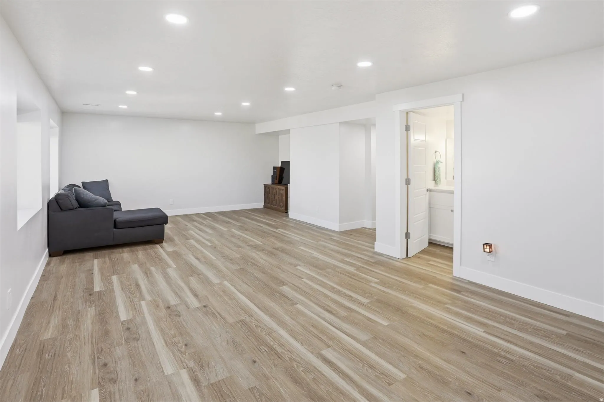 Spacious room featuring light wood-finish flooring, recessed lighting, and a white color palette