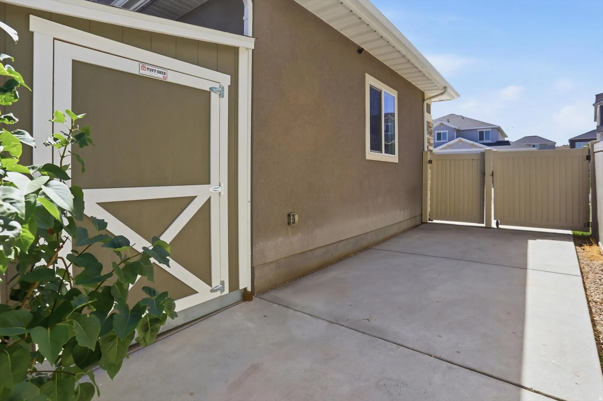 Side yard featuring a concrete pad, a storage shed with a white trim door, and a privacy fence with a double gate
