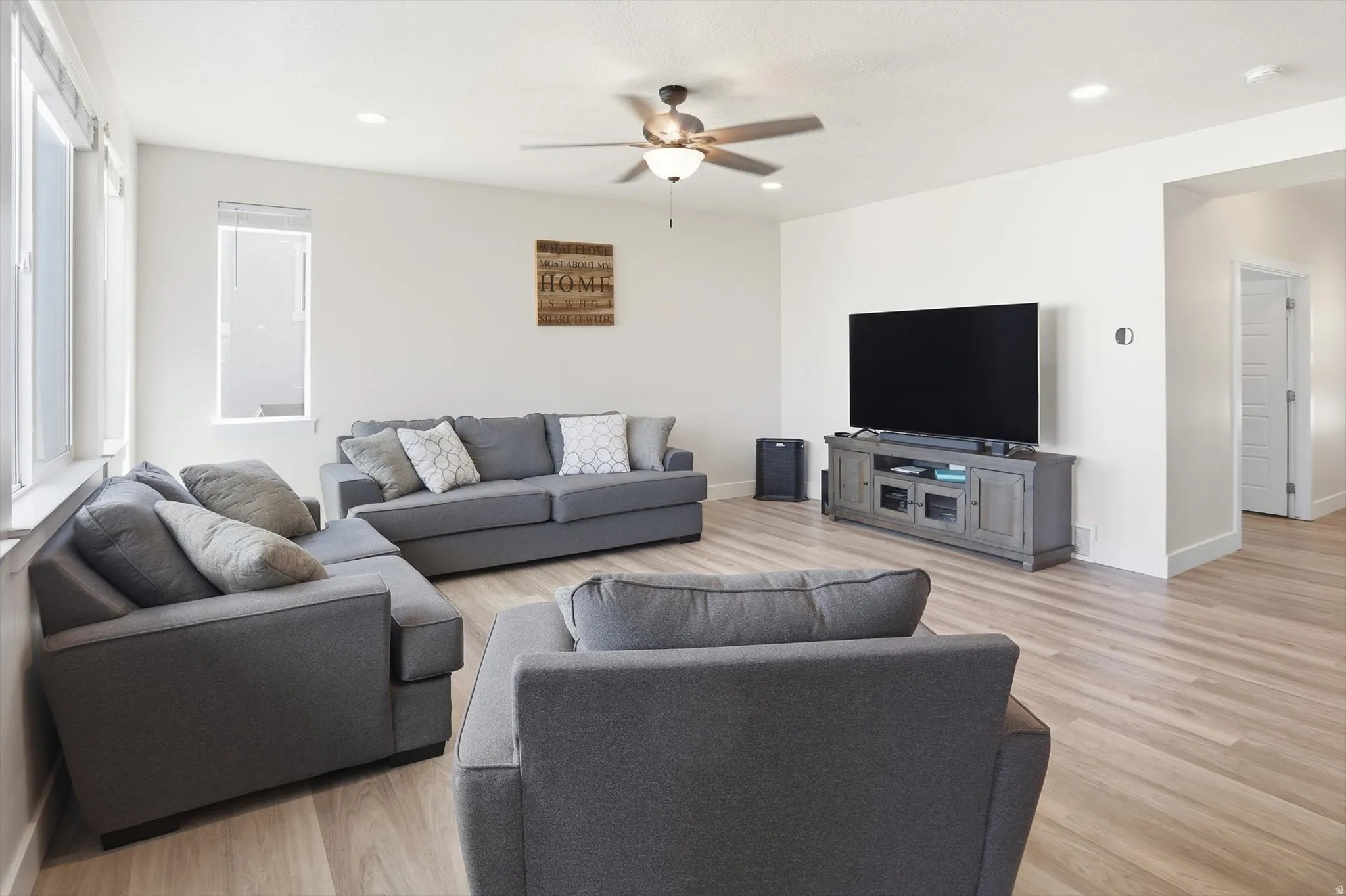 Open-concept living area featuring light wood-finish flooring, recessed lighting, a ceiling fan, multiple windows, and crisp white walls