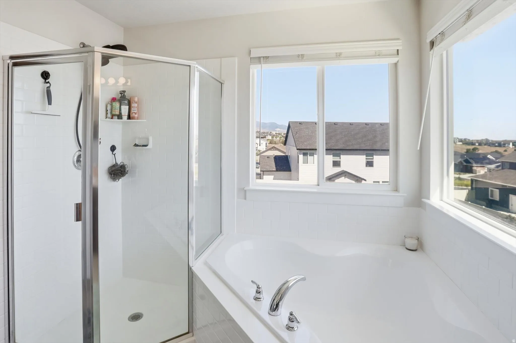 Corner soaking tub with polished chrome fixtures, surrounded by white tile and large windows