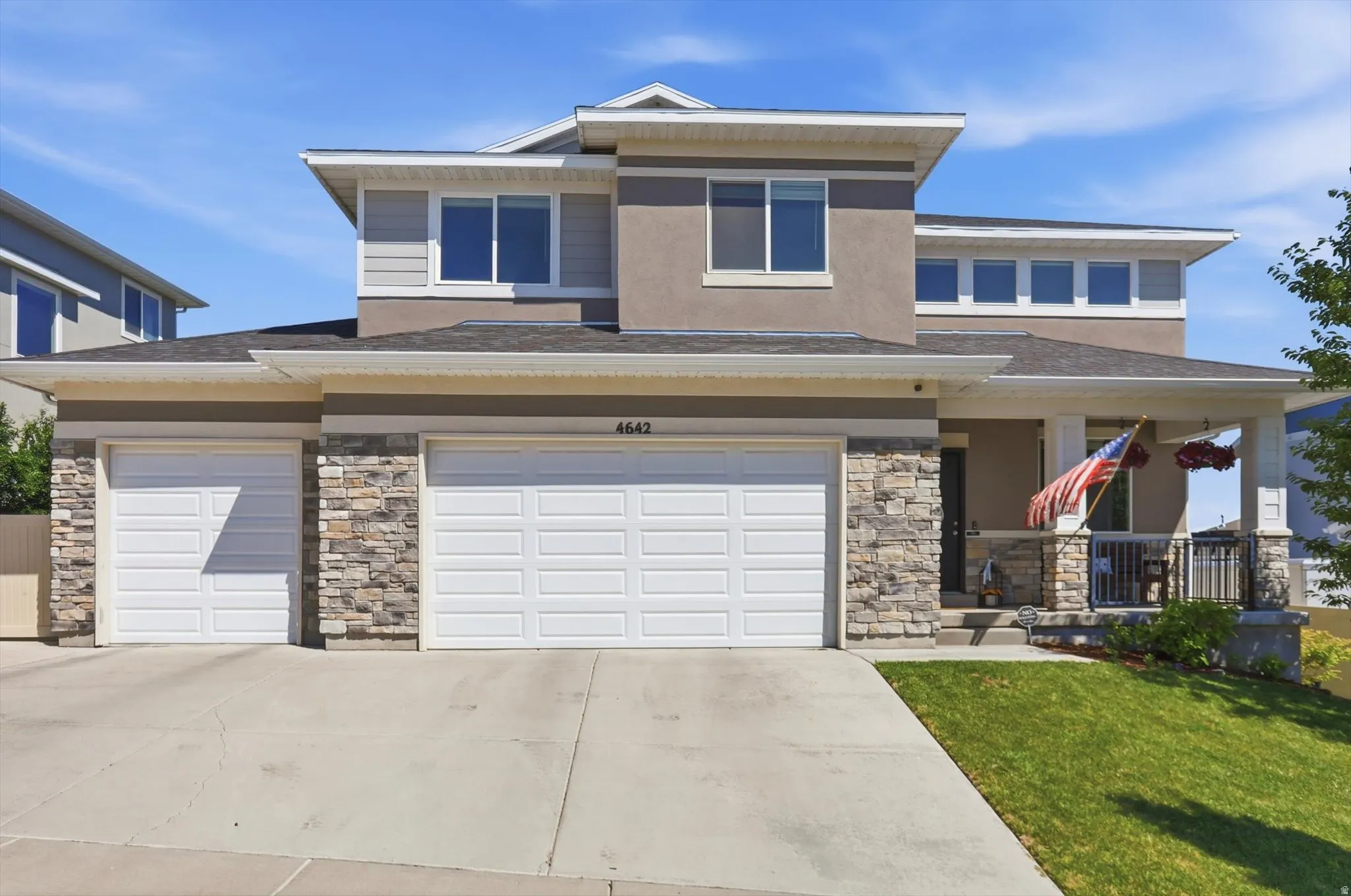 Contemporary multi-story residence featuring a two-car garage, stone facade accents, a covered front porch, and upper-level windows