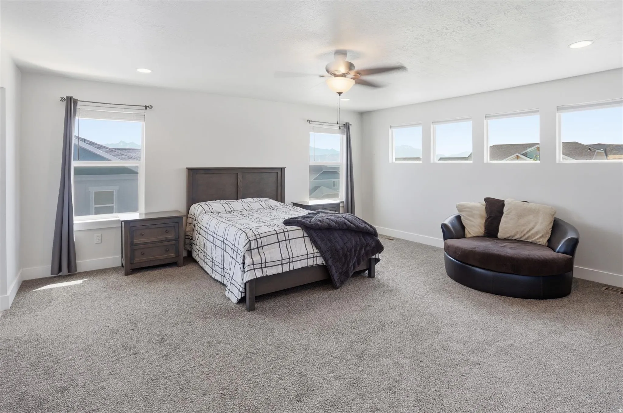 Spacious room featuring neutral carpeting, recessed lighting, a ceiling fan, and multiple windows providing natural illumination