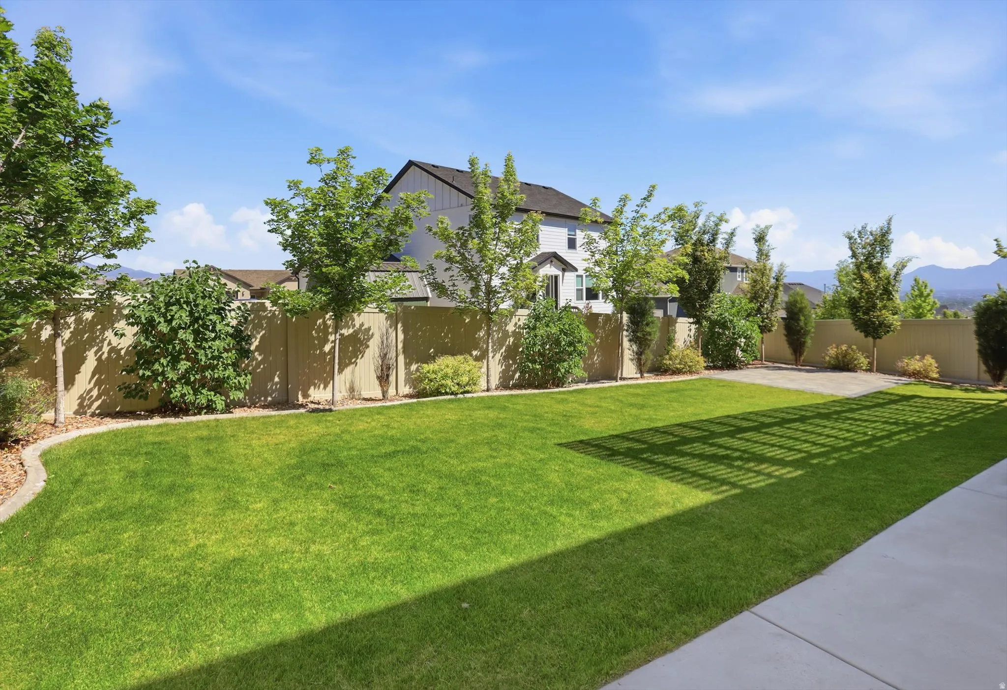 Spacious backyard featuring a manicured lawn, established trees, perimeter fencing, and a concrete patio