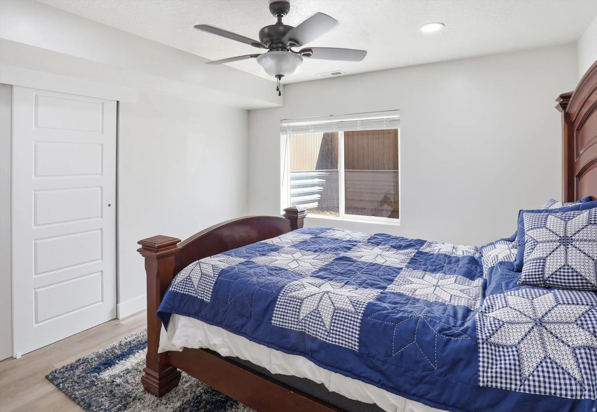 Bright room featuring wood-finish flooring, a white five-panel sliding door, and a modern ceiling fan with integrated lighting