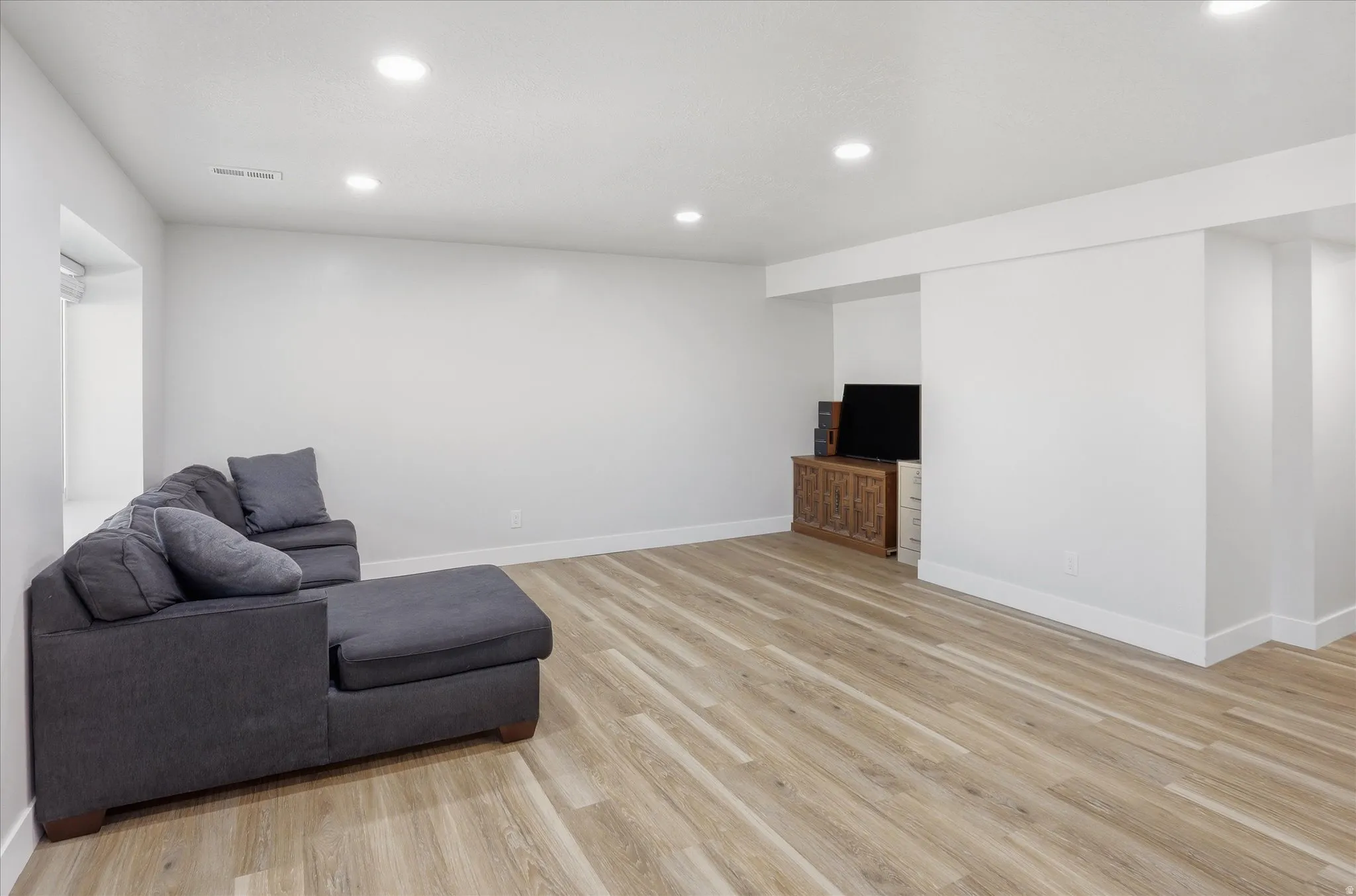 Spacious room featuring wood-finish flooring, recessed ceiling lighting, crisp white walls, and a large window opening