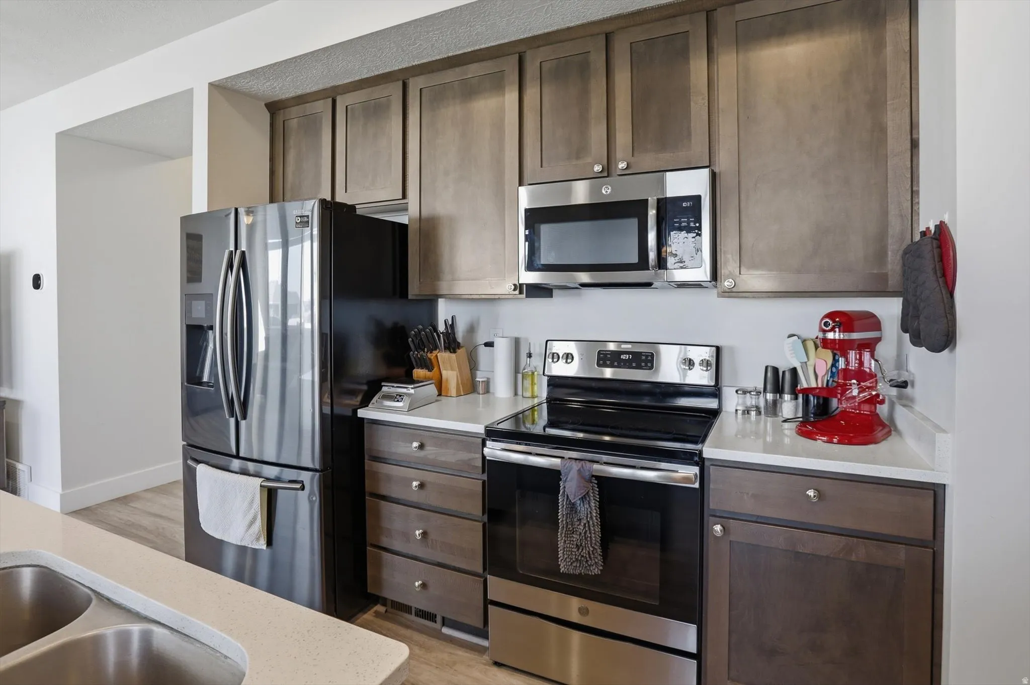 Kitchen featuring stainless steel appliances, wood-finish cabinetry, light-toned countertops, a dual basin sink, and an over-the-range microwave