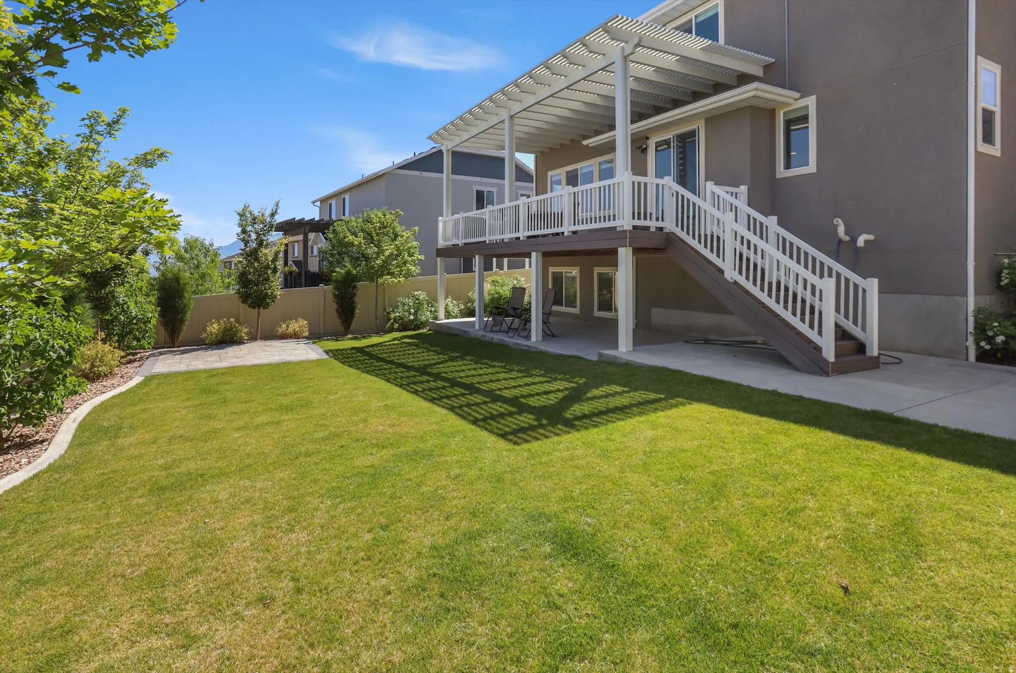 Expansive backyard with a manicured lawn, a raised composite deck with white railings, and a covered patio area below