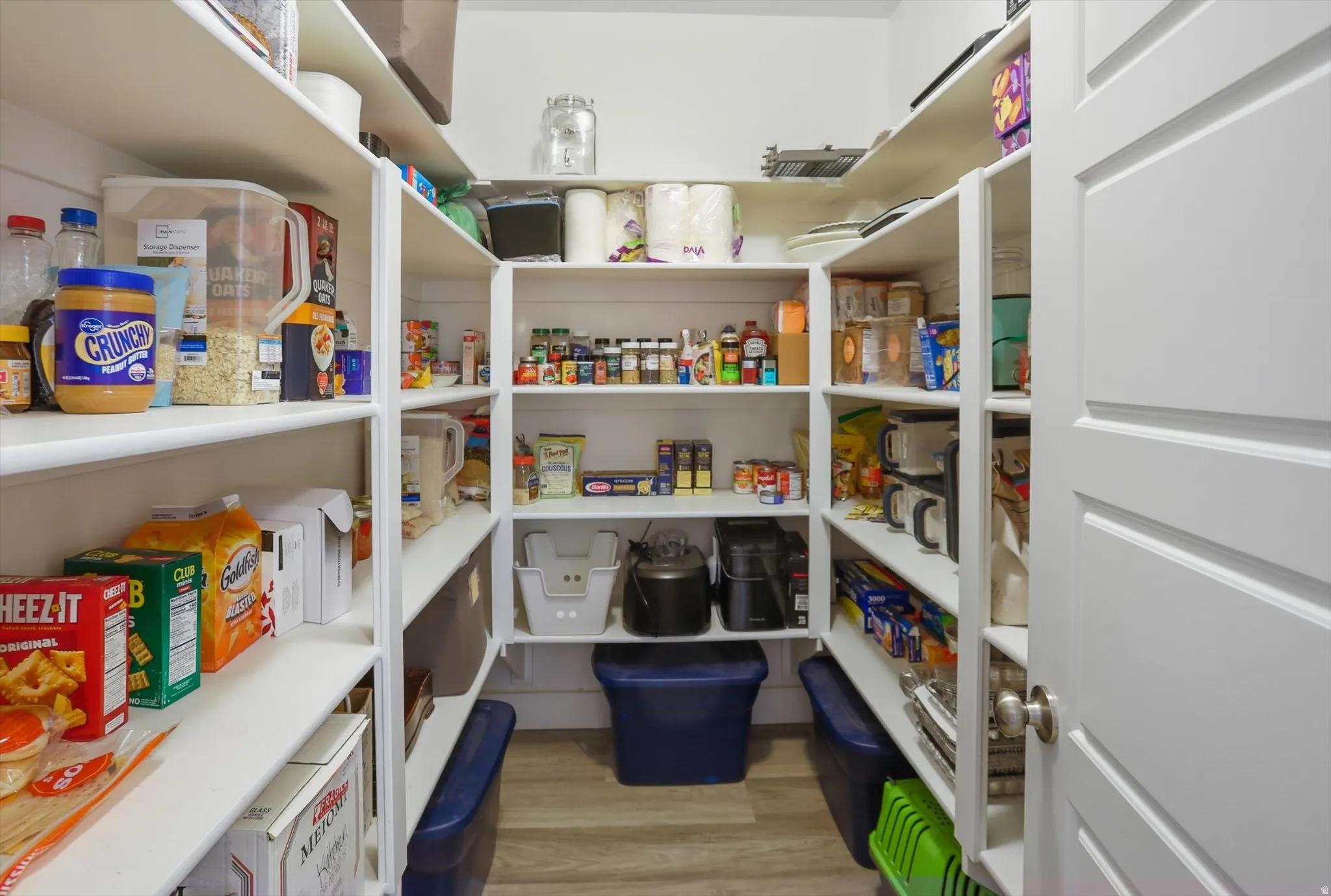 Walk-in pantry featuring extensive white shelving, wood-finish flooring, and a paneled door with a brushed nickel knob
