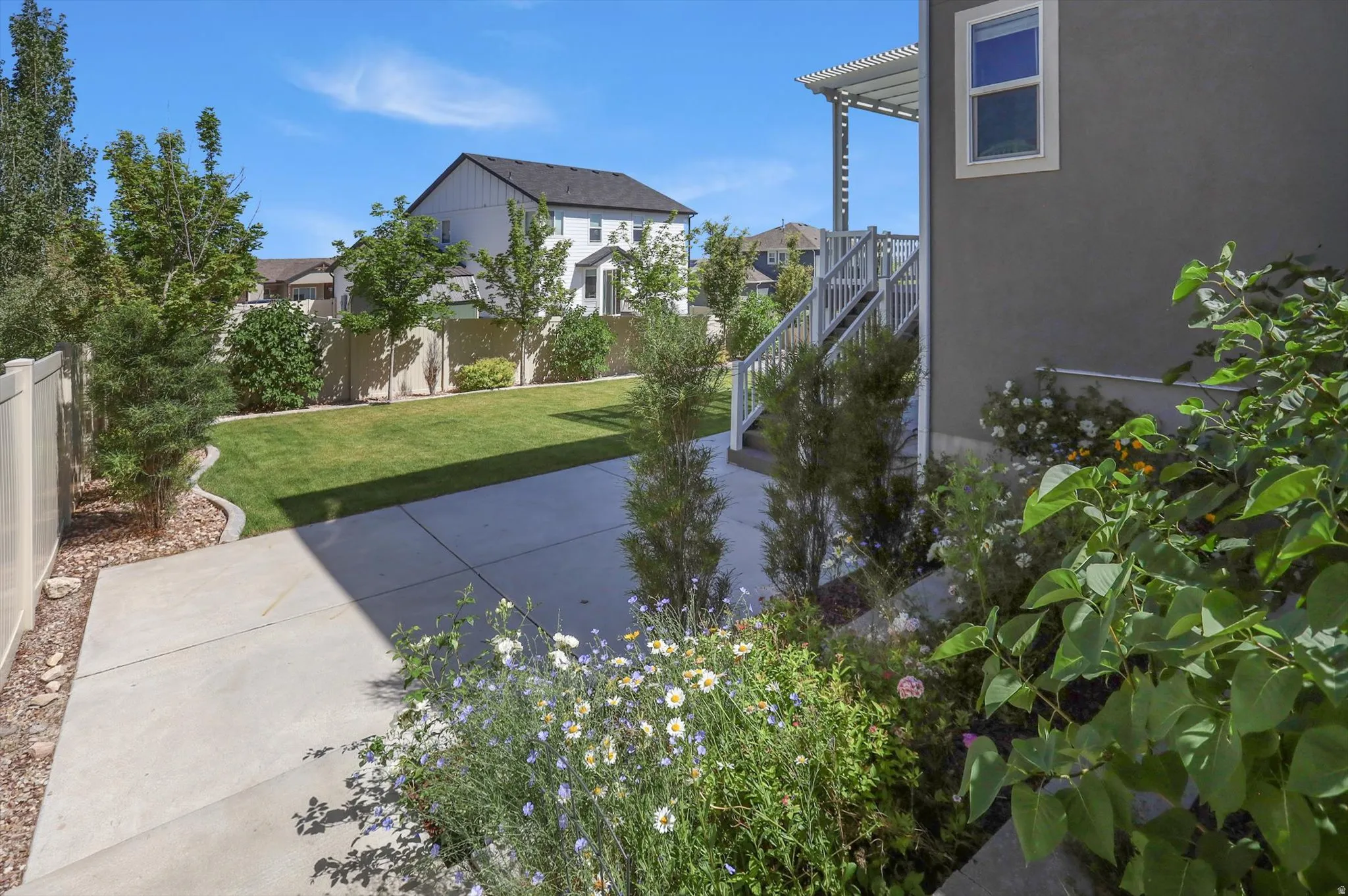 Expansive backyard featuring a manicured lawn, concrete patio, privacy fencing, mature trees, and established plantings