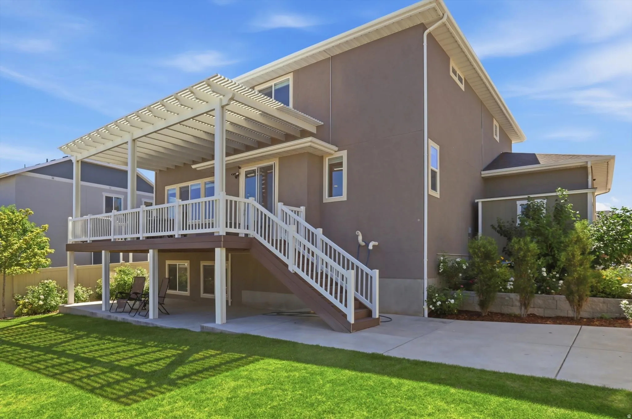 Expansive backyard featuring a manicured lawn, a large upper-level deck with a pergola, a stairway with white railings, a lower-level concrete patio, and mature landscaping