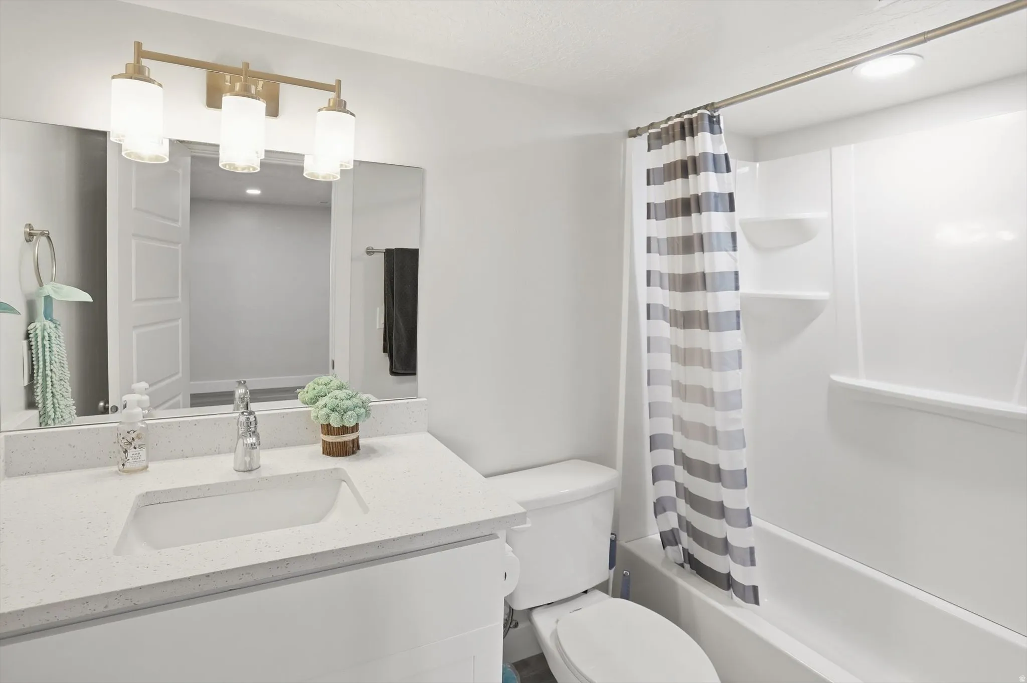 Bathroom featuring a white vanity with an integrated sink, a light-colored countertop, and a gold-finish three-light fixture
