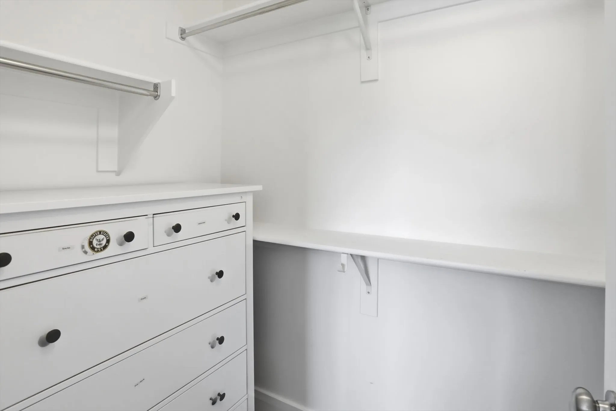Closet system featuring a built-in dresser with black knobs, multiple shelving units, and chrome hanging rods