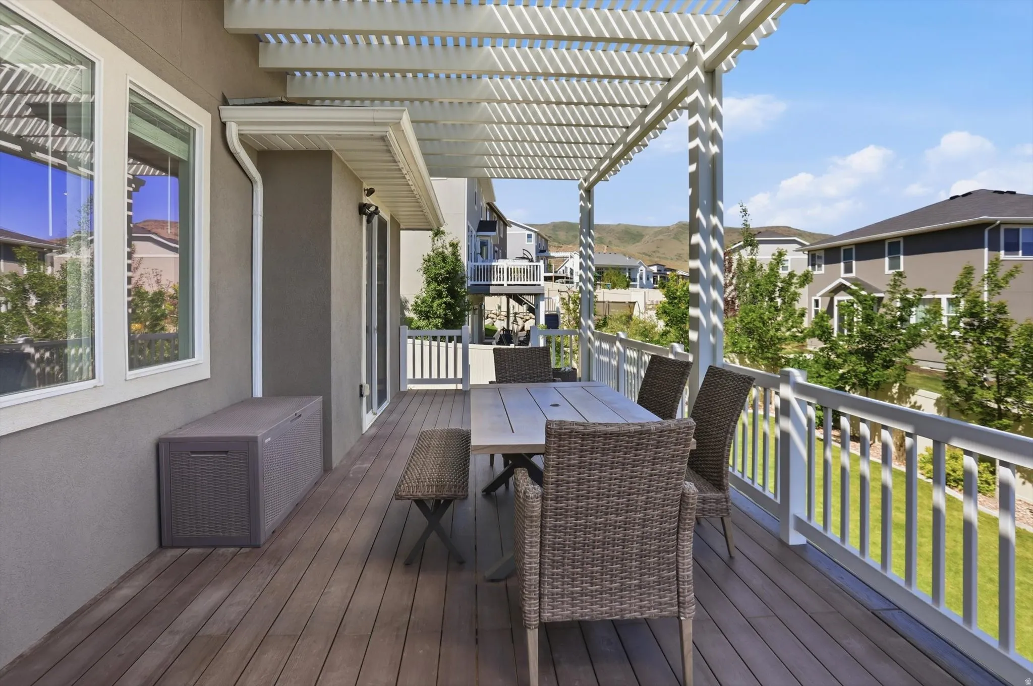 Expansive outdoor deck featuring wood-finish flooring, a white slatted pergola, and a white baluster railing
