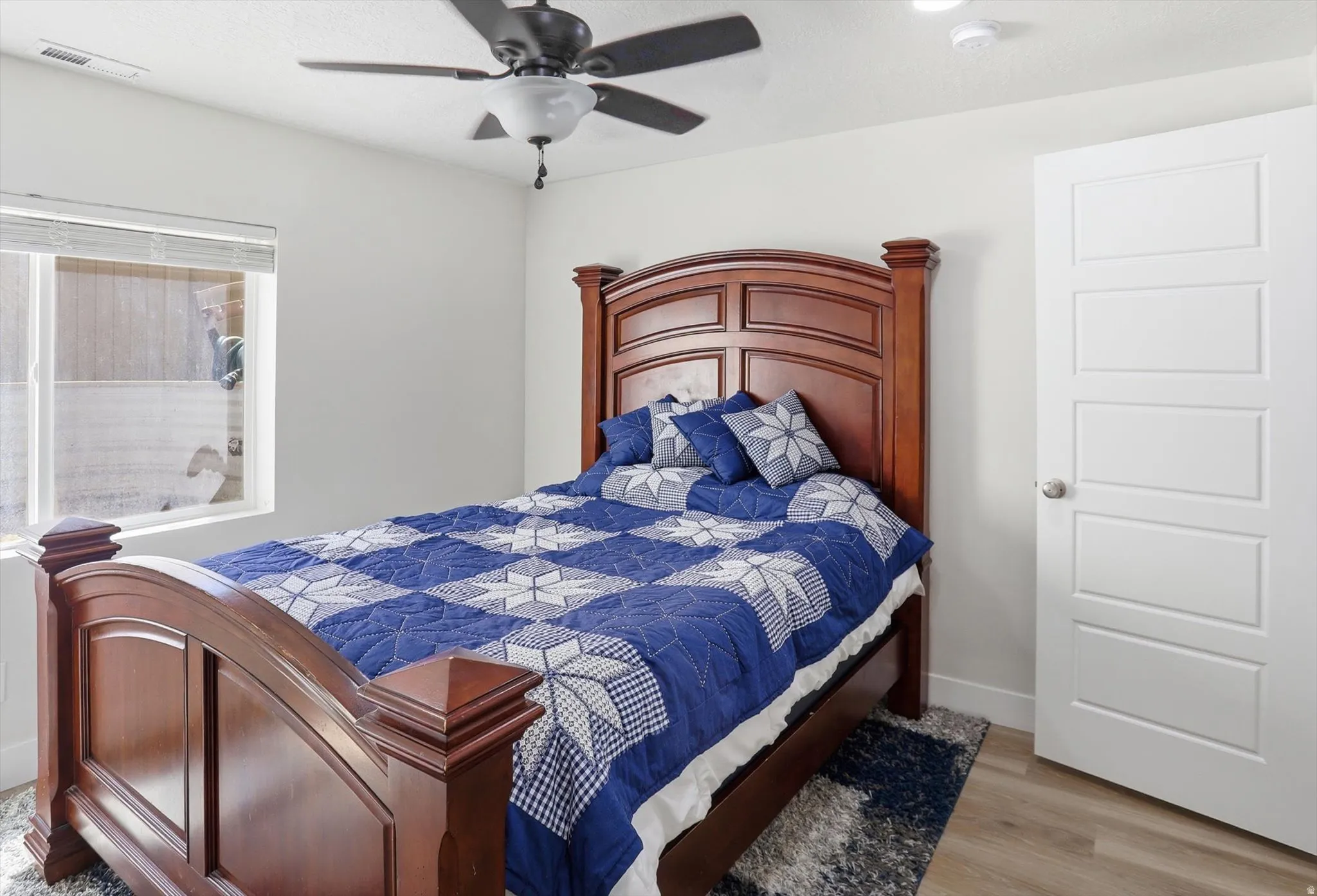 Bright interior space featuring a window with blinds, wood-finish flooring, a contemporary ceiling fan, and a four-panel interior door