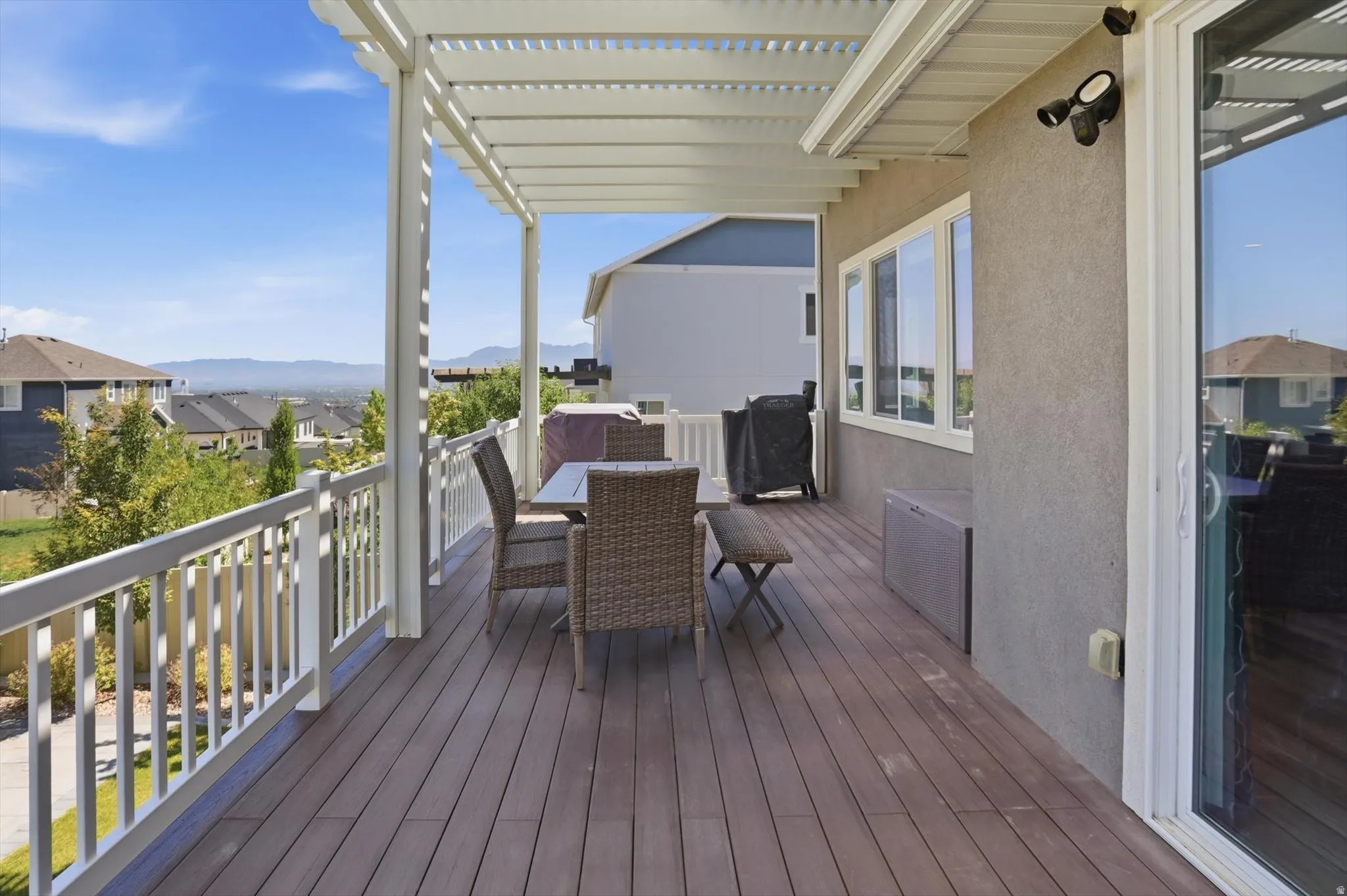 Expansive outdoor deck featuring wood-finish flooring, a full pergola, white railing, and a sliding glass door entry