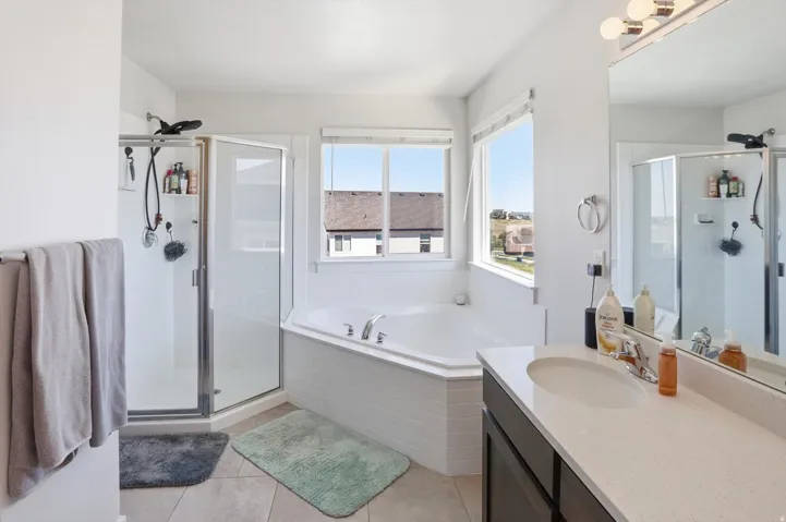 Bathroom featuring a built-in corner soaking tub, separate glass-enclosed shower, single vanity with a solid surface countertop, and large mirror with overhead lighting