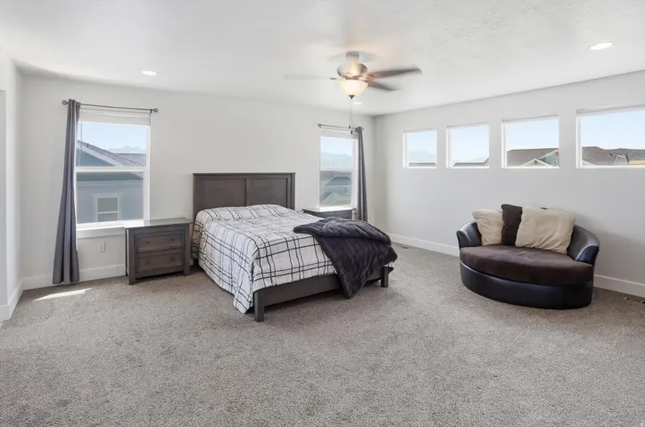 Spacious room featuring neutral carpeting, recessed lighting, a ceiling fan, and multiple windows providing natural illumination