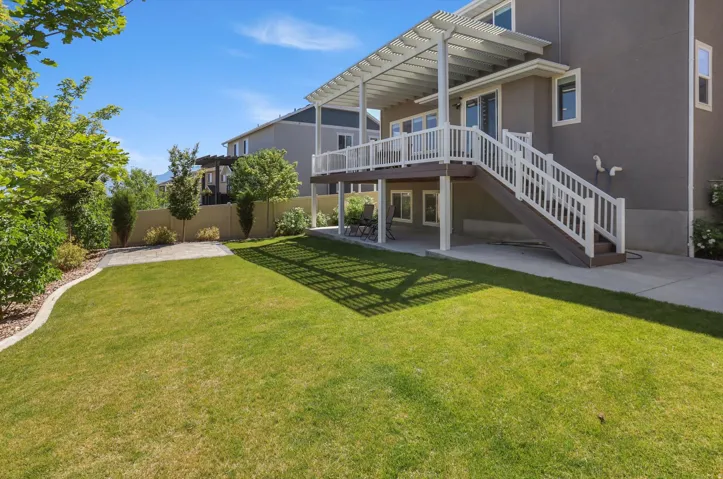 Expansive backyard with a manicured lawn, a raised composite deck with white railings, and a covered patio area below