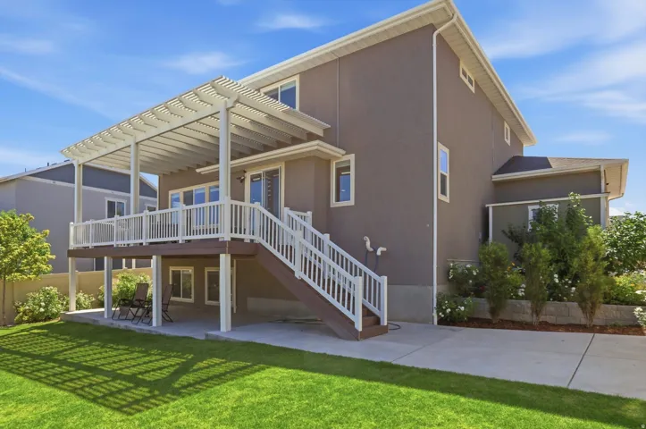 Expansive backyard featuring a manicured lawn, a large upper-level deck with a pergola, a stairway with white railings, a lower-level concrete patio, and mature landscaping