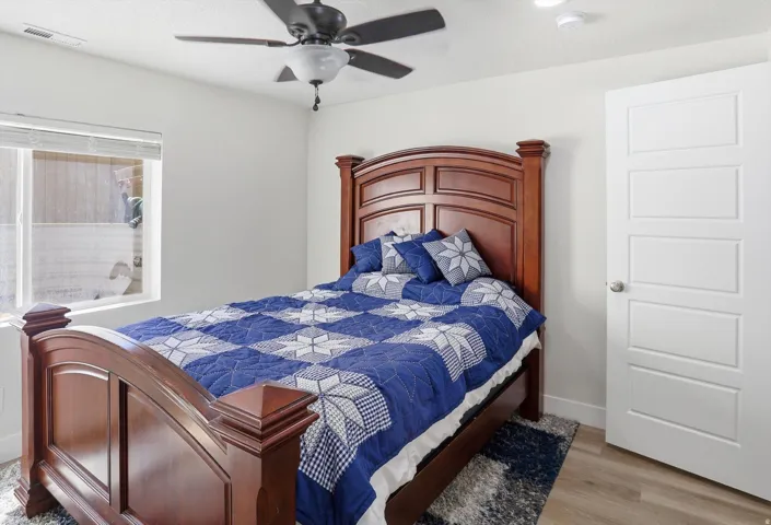 Bright interior space featuring a window with blinds, wood-finish flooring, a contemporary ceiling fan, and a four-panel interior door