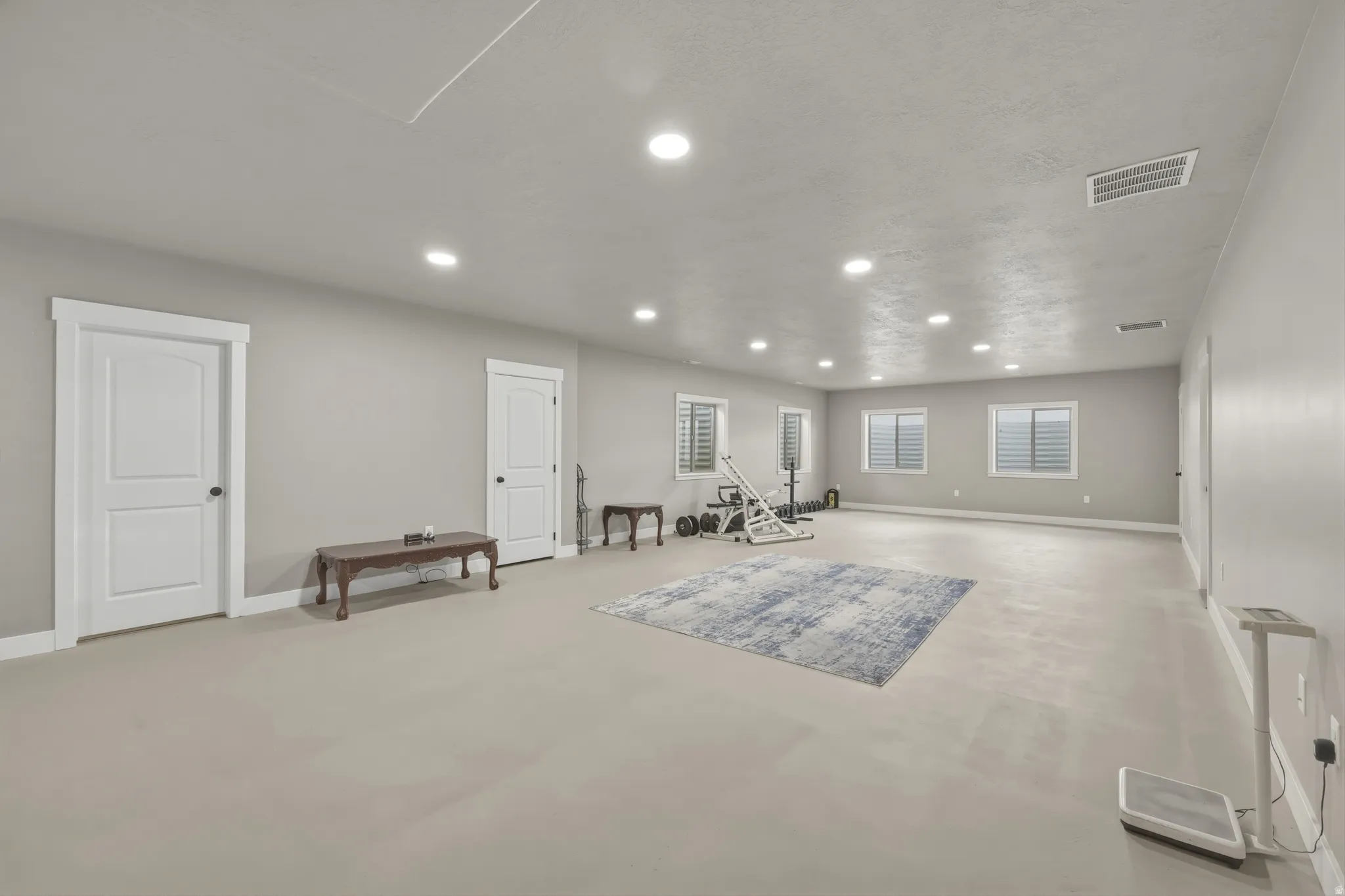 Spacious room featuring light gray walls, recessed lighting, and multiple windows with horizontal blinds
