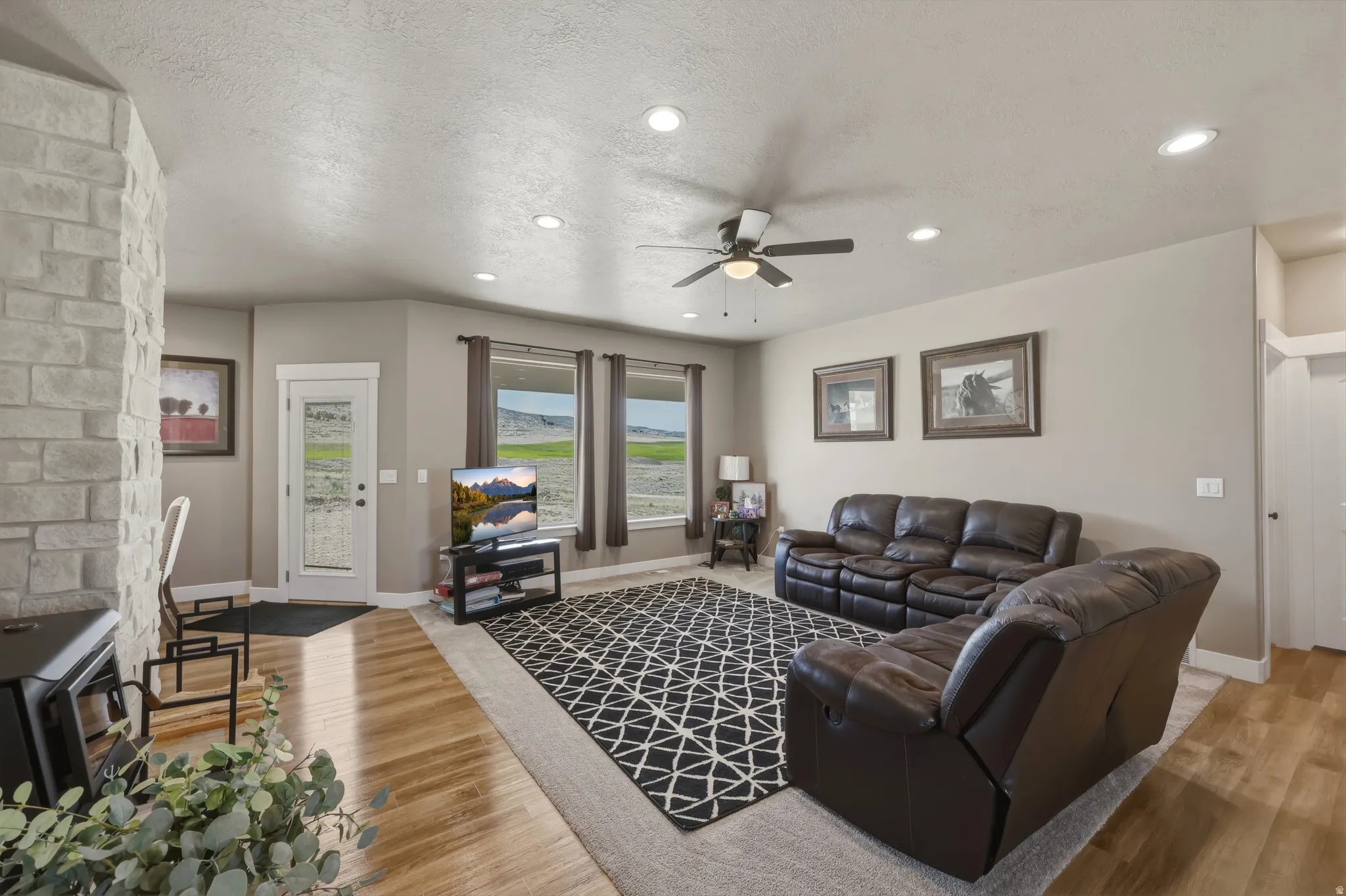 Open-concept living area featuring wood-finish flooring, a stone-clad hearth, recessed lighting, and a ceiling fan