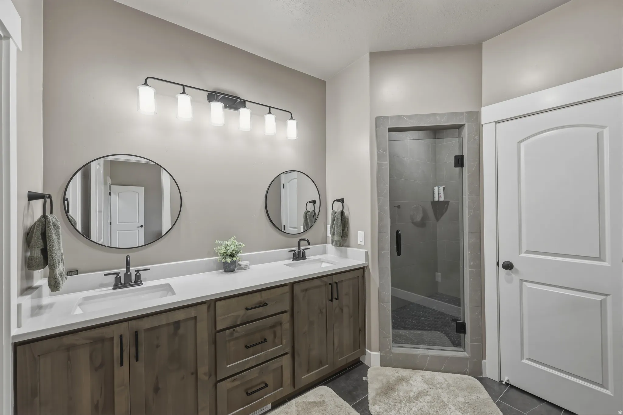 Dual vanity with wood-finish cabinetry, white countertops, and matte black fixtures