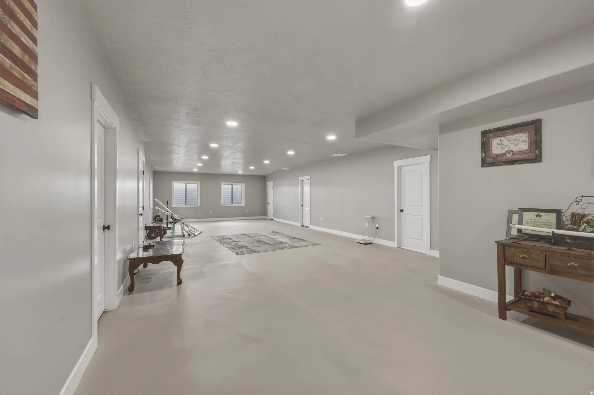 Expansive finished lower level featuring light gray walls, recessed lighting, multiple white paneled doors with dark hardware, and three windows
