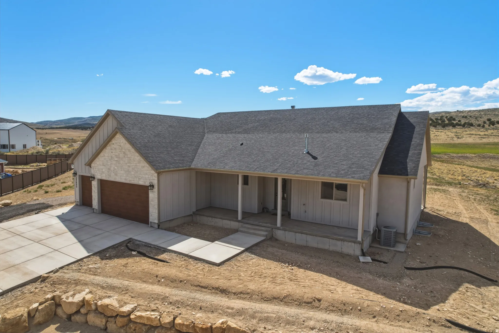 Modern ranch-style residence featuring a two-car garage with wood-finish doors, a covered front porch, and durable asphalt shingle roofing