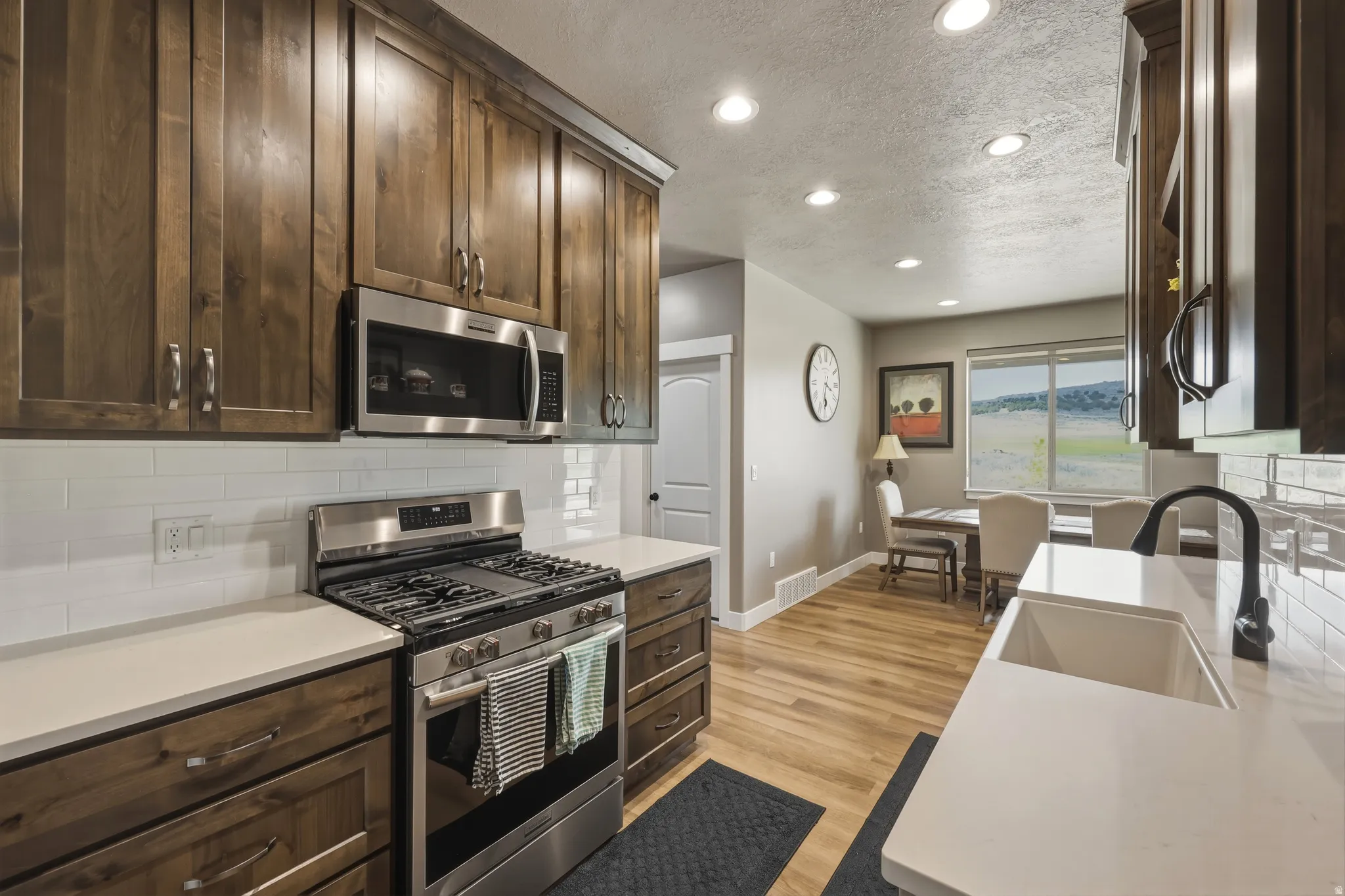Kitchen featuring dark wood-finish cabinetry, stainless steel appliances, a white subway tile backsplash, and light-toned countertops