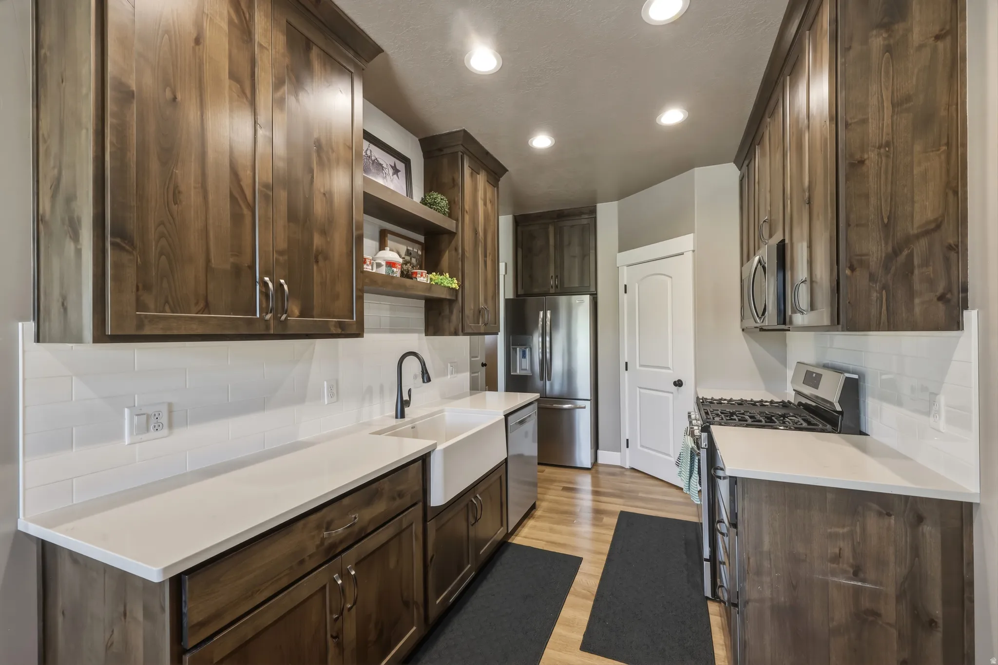 Kitchen featuring rich wood cabinetry, stainless steel appliances, a farmhouse-style sink with a matte black faucet, light countertops, and subway tile backsplash