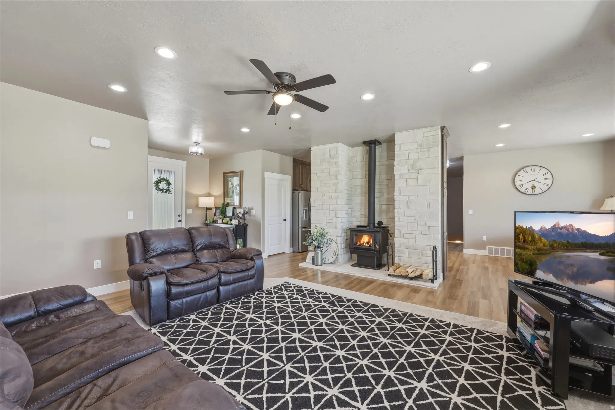 Living area featuring a stone accent wall with a wood-burning stove, light wood-finish flooring, and recessed lighting