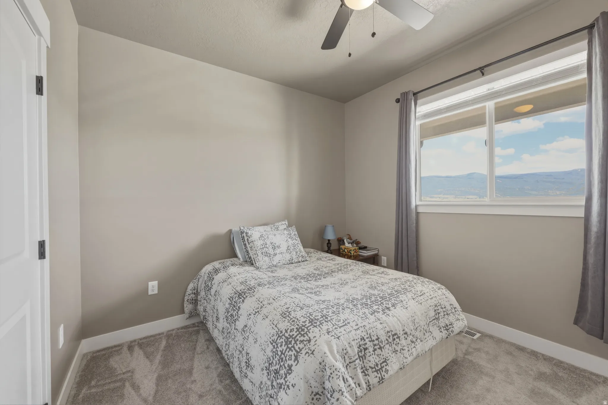 Bedroom featuring neutral wall color, grey carpet, ceiling fan, and a window with mountain scenery