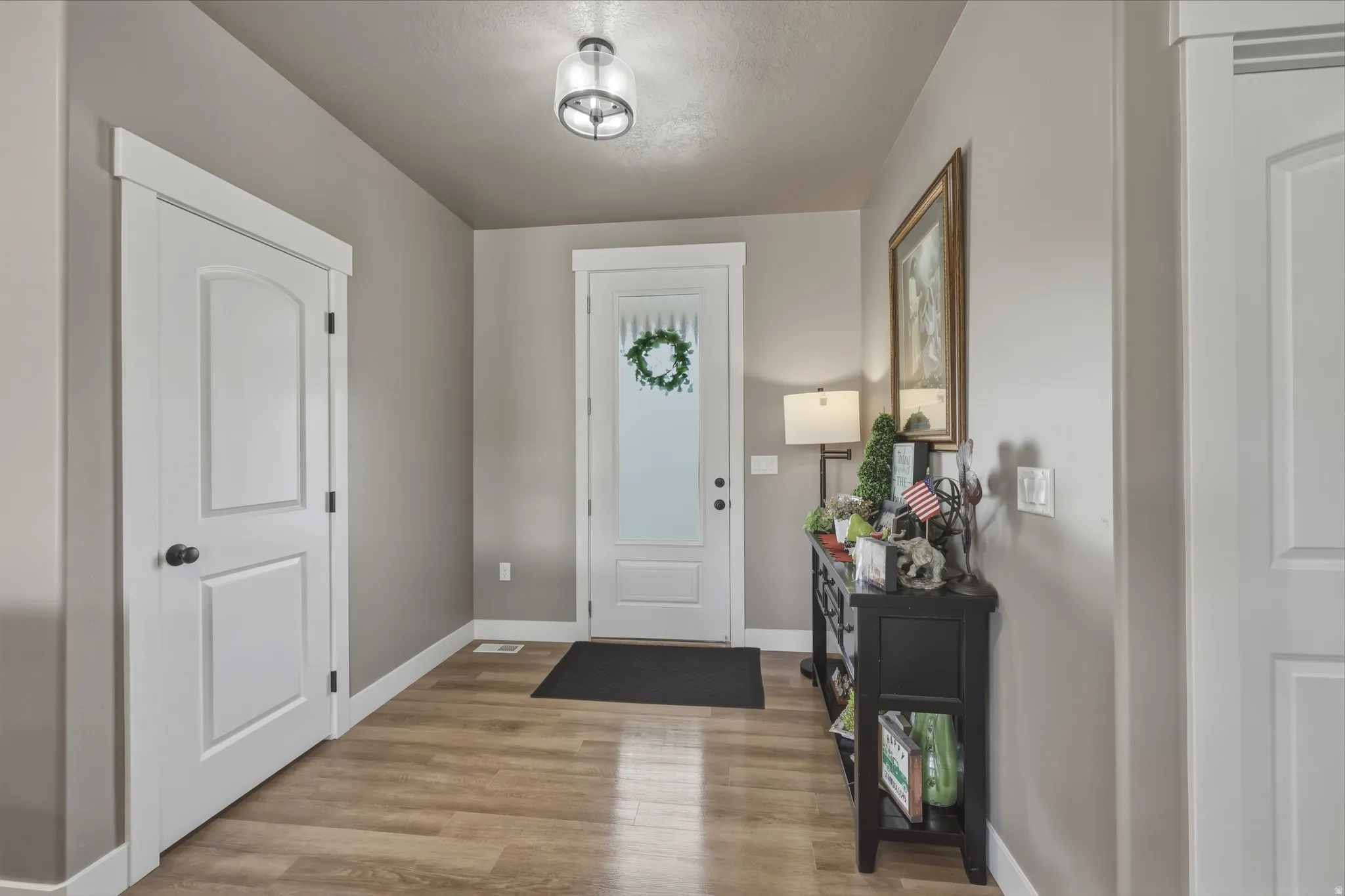 Entryway featuring wood-finish flooring, a white paneled door with black hardware, and a frosted glass front door