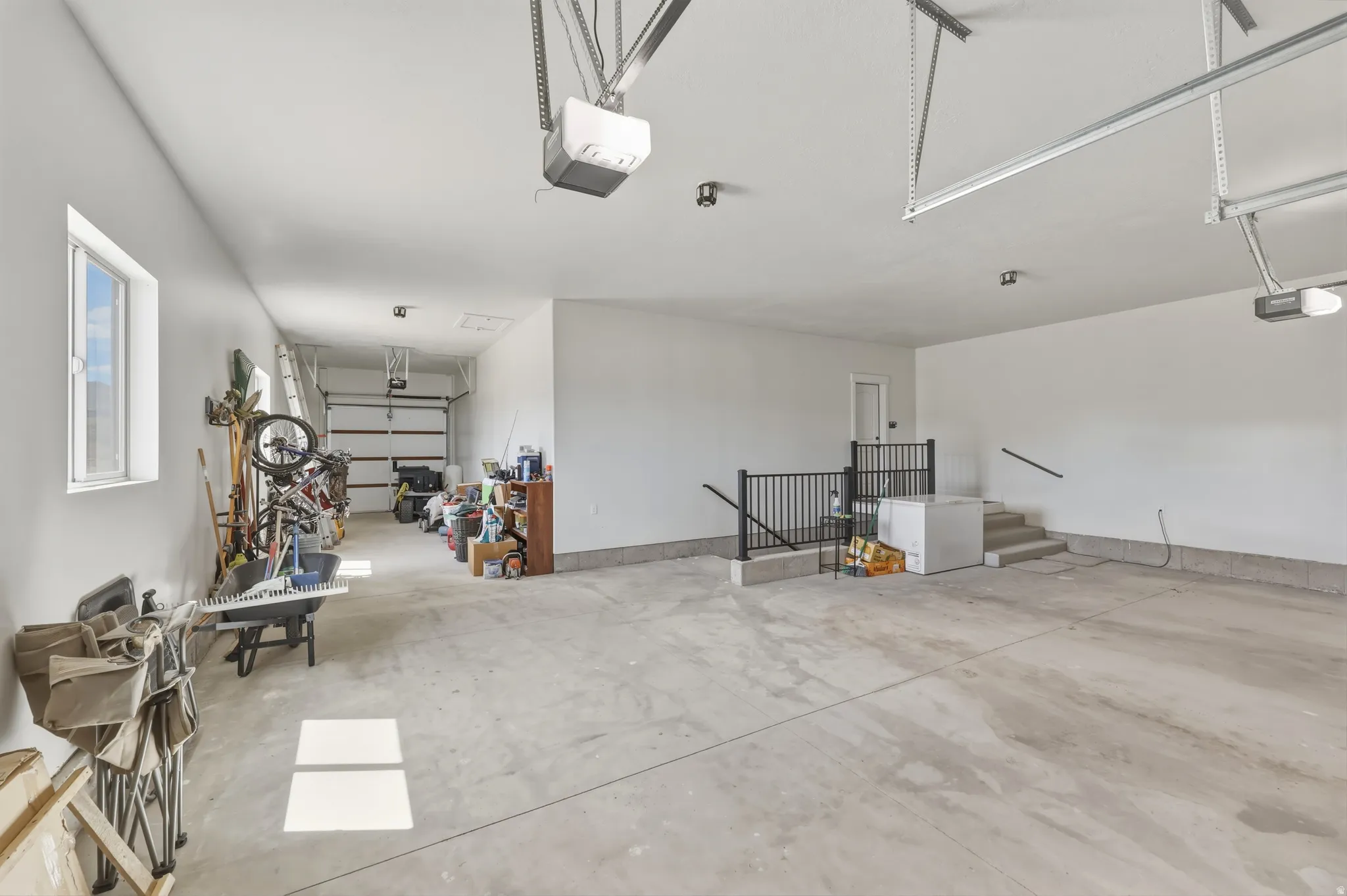 Spacious garage with multiple overhead doors, concrete flooring, and an interior staircase featuring a black metal railing