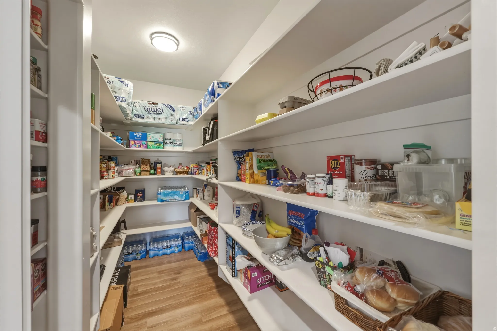 Spacious walk-in pantry featuring extensive built-in shelving, wood-finish flooring, and overhead flush-mount lighting