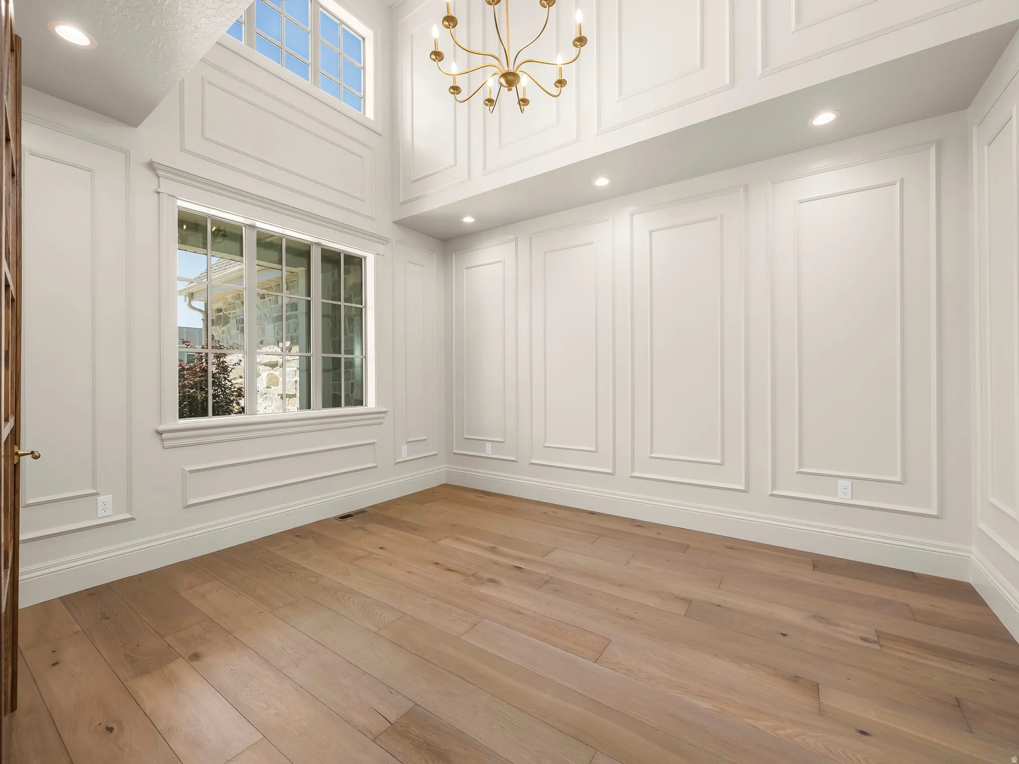 Spacious room featuring wood-finish flooring, wainscoting, high ceilings, recessed lighting, and a brass chandelier