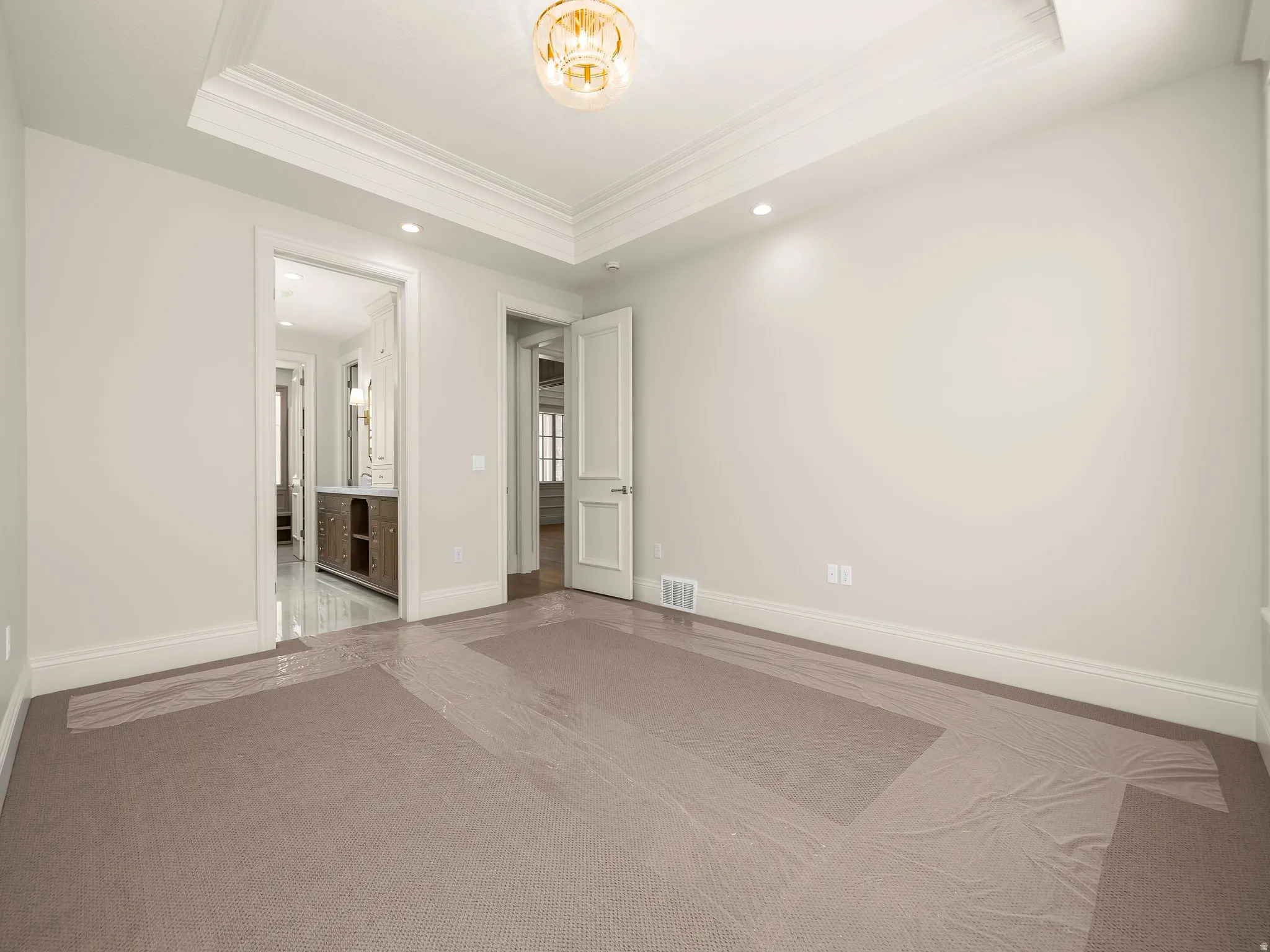 Spacious room featuring neutral carpeting, extensive crown molding, a tray ceiling with an ornamental light fixture, and recessed lighting