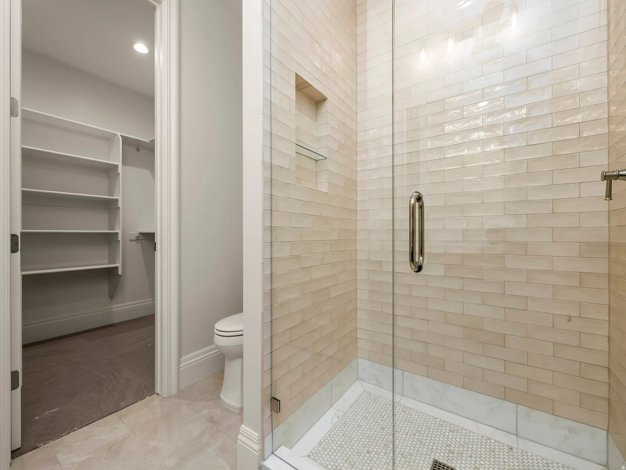Glass-enclosed shower with subway tile surround and mosaic tile flooring