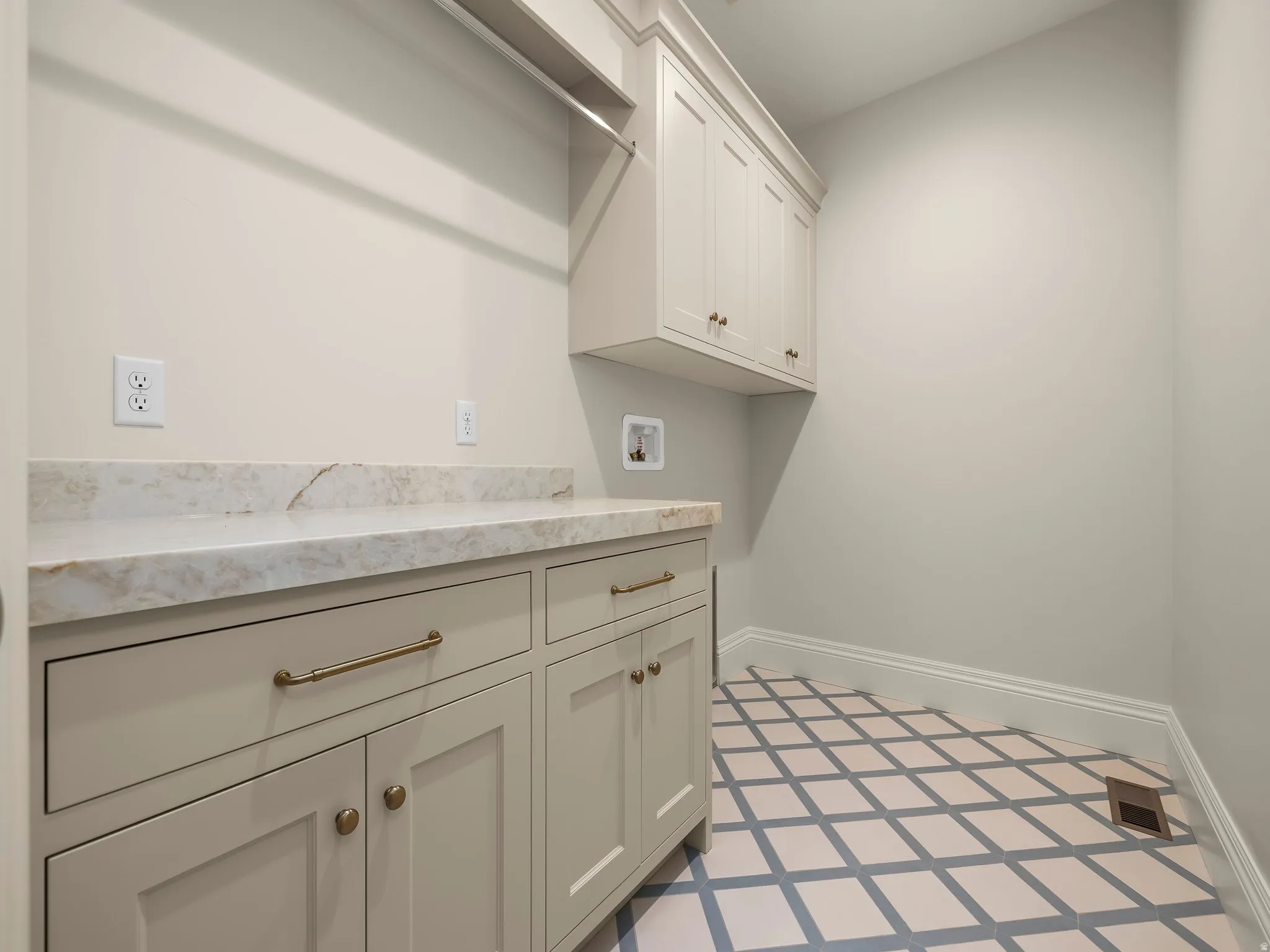 Utility room featuring custom cabinetry, a stone-finish countertop, patterned tile flooring, and integrated wall shelving with a hanging rod