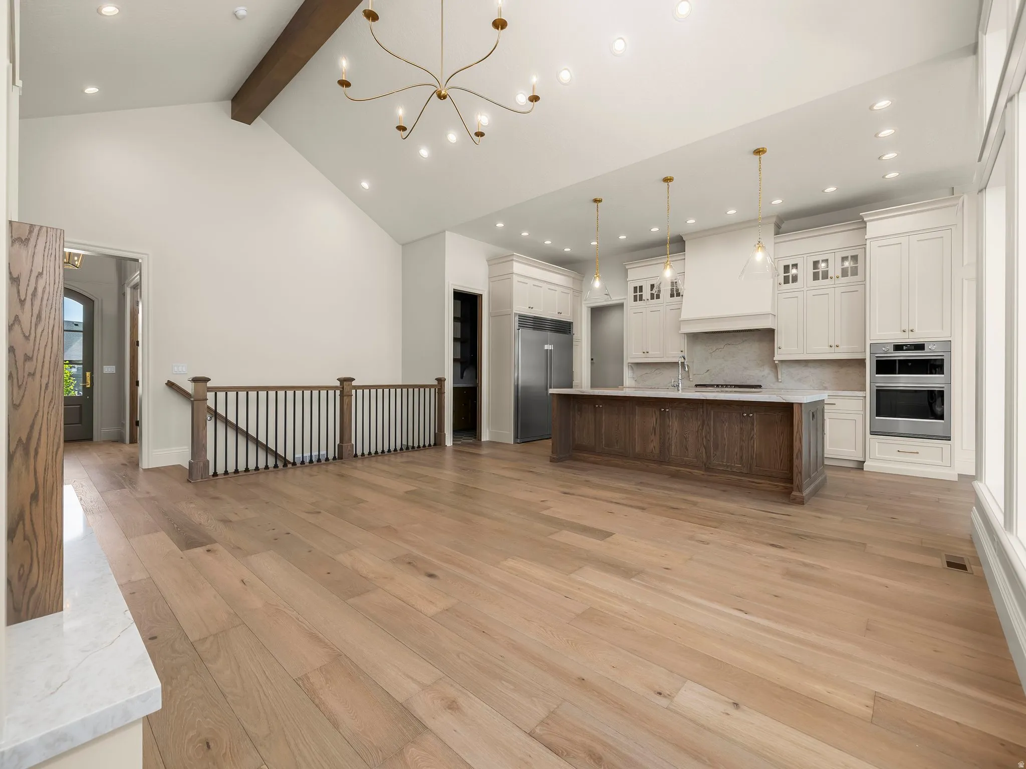 Spacious open-concept living area featuring light wood-finish flooring and a vaulted ceiling with an exposed wood beam