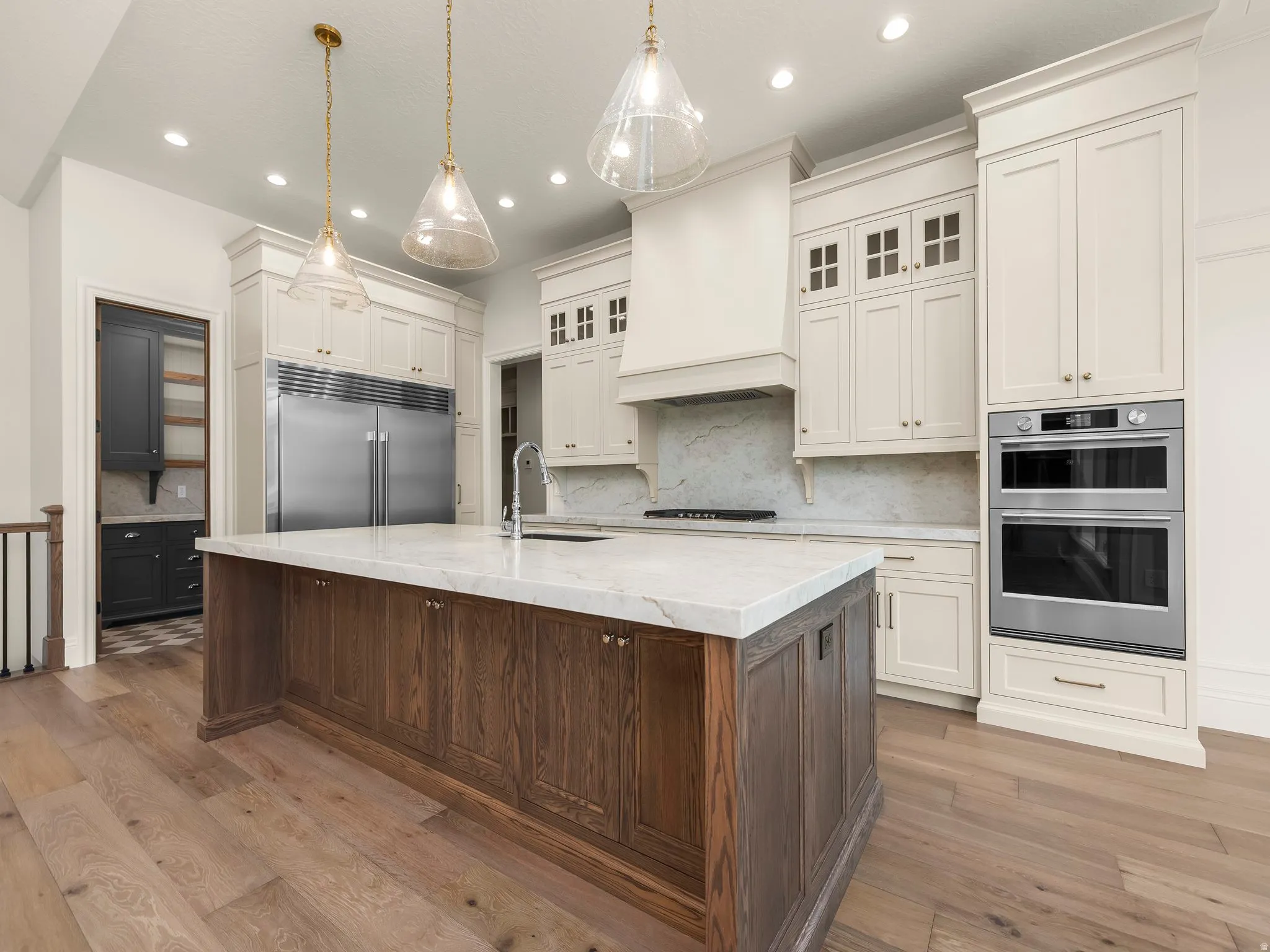 Spacious kitchen featuring a large wood-finish island with a light-toned countertop, integrated stainless steel appliances, extensive cream cabinetry, and light wood-finish flooring