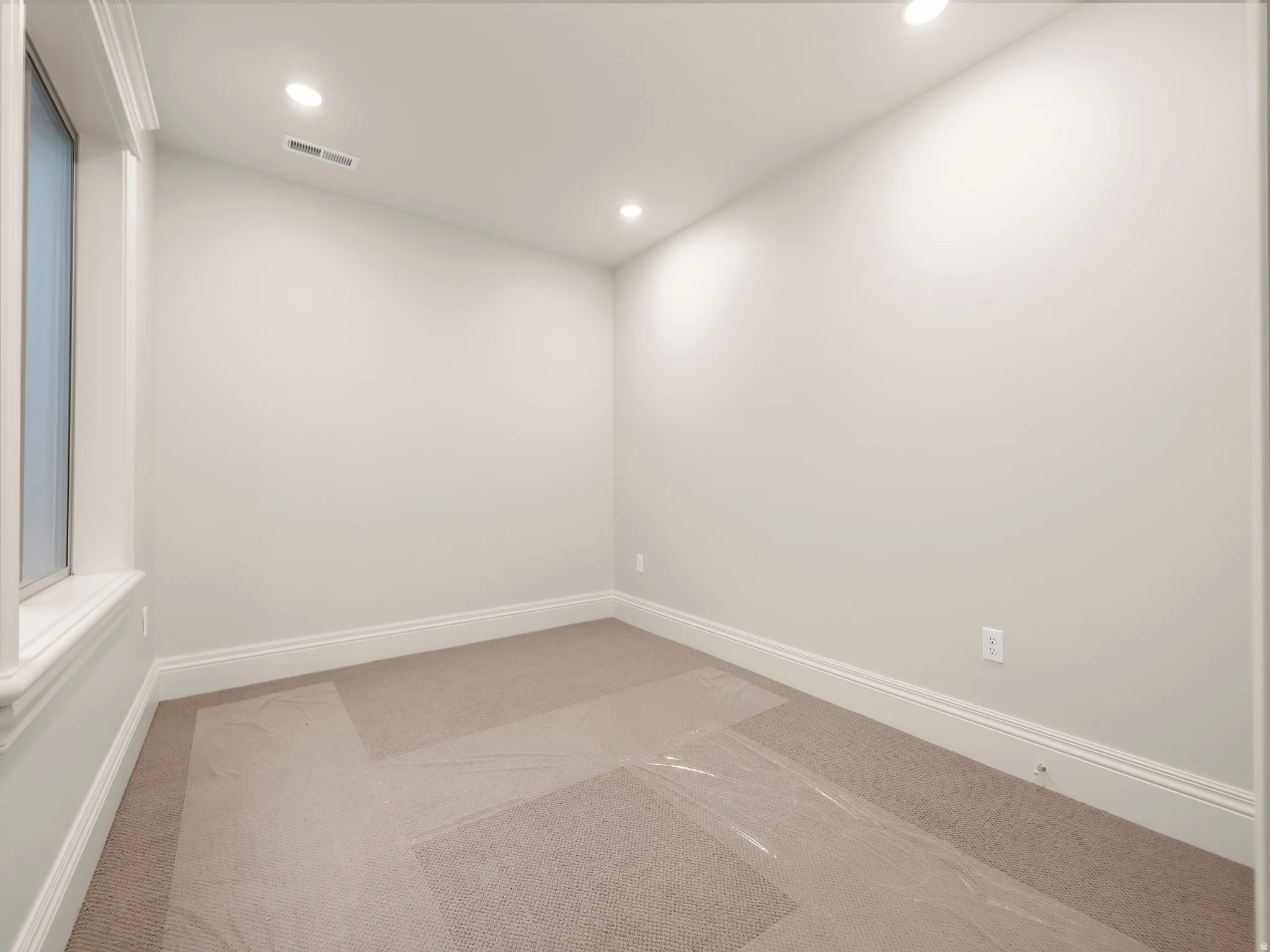Recessed lighting illuminates neutral-toned walls and plush carpeting, featuring white trim work and a single window